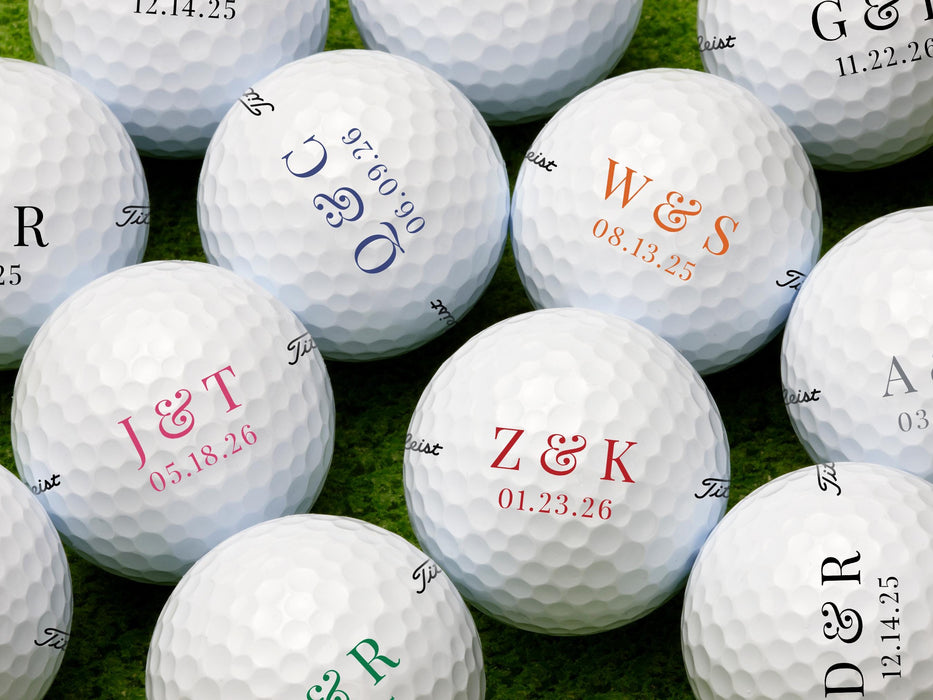 Multiple Titleist golf balls shown with different initials, dates, and colors on each ball. Golf balls sit on a grassy surface.
