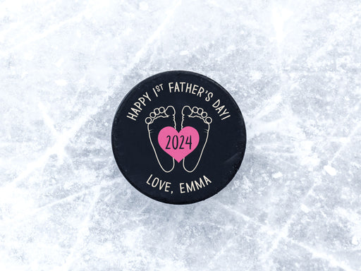 hockey puck ontop of ice with pink 1st Fathers Day footprint design with the name Emma printed on it