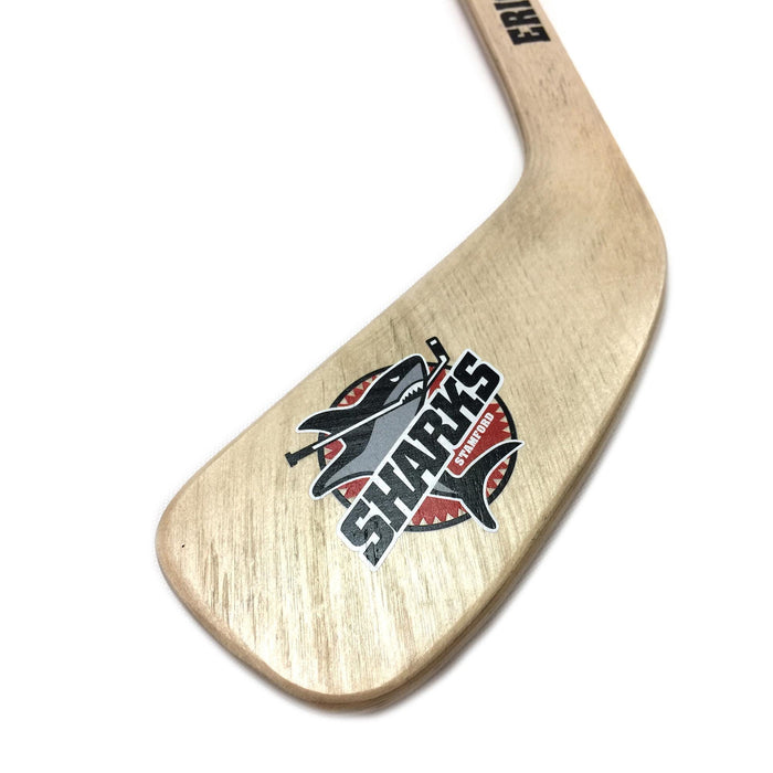 Close-up of a hockey stick blade featuring a detailed multicolor team logo design printed on the wood surface.