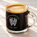 A glass mug filled with a dark liquid, likely coffee, with a foamy top. The mug has a personalized message engraved on it, which reads "Happy Mother's Day 2026 LOVE, REED".