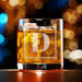 Elegant product photo of the engraved whiskey glass against a soft bokeh background. The framed initial design is centered and clearly visible.