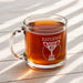 A glass mug filled with a brown liquid, likely tea, sits on a wooden surface.