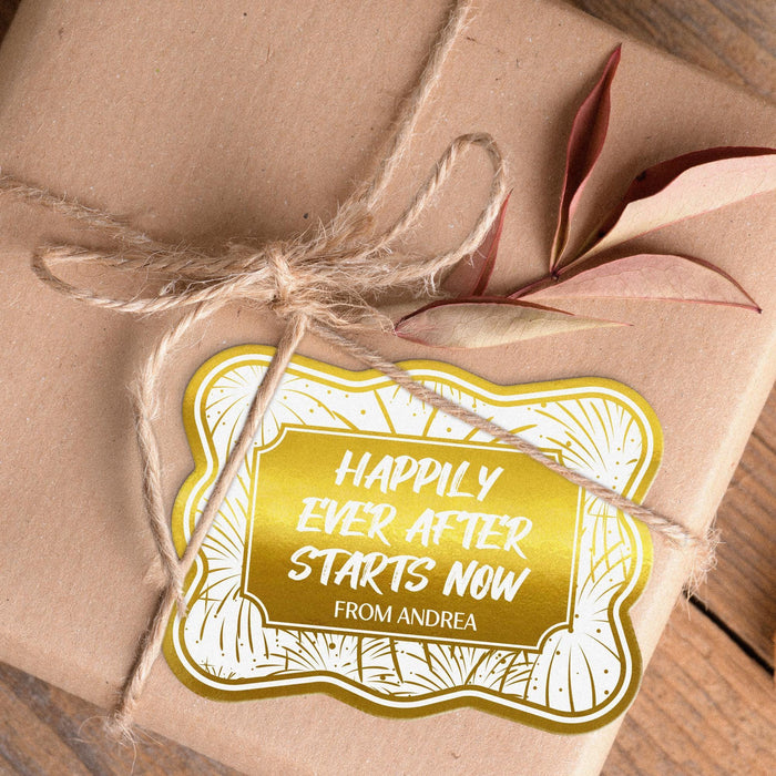 Close-up of a personalized wedding gift tag featuring the “Happily Ever After Starts Now” design in gold foil. The custom cardstock tag is tied with twine to a wrapped gift, showcasing the elegant wedding-inspired artwork and personalized sender name.