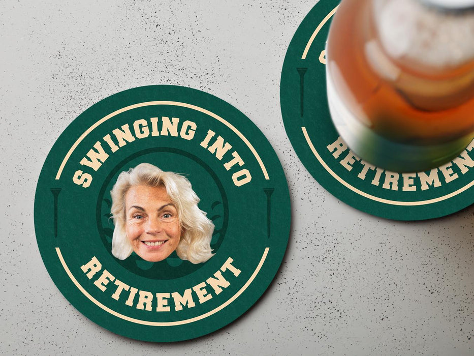 Custom round pulpboard coasters are shown sitting on a light gray stone background with a beer glass on top of one. The custom coasters feature design printed with playful &quot;Swinging Into Retirement&quot; text, golf imagery, and custom photo.