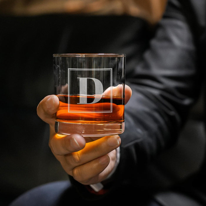 Close-up lifestyle photo of a personalized whiskey glass held in hand, showcasing the framed initial engraving. The glass is filled with whiskey and ice, ideal for gifting.