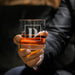 Close-up lifestyle photo of a personalized whiskey glass held in hand, showcasing the framed initial engraving. The glass is filled with whiskey and ice, ideal for gifting.