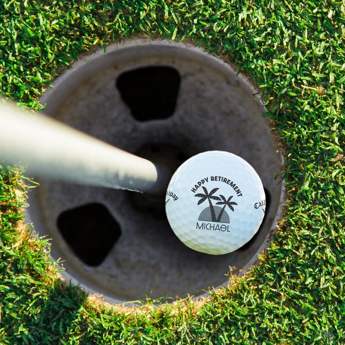 Top view of a personalized retirement golf ball resting in a golf cup. Features the Happy Retirement Palm Trees design and custom name.