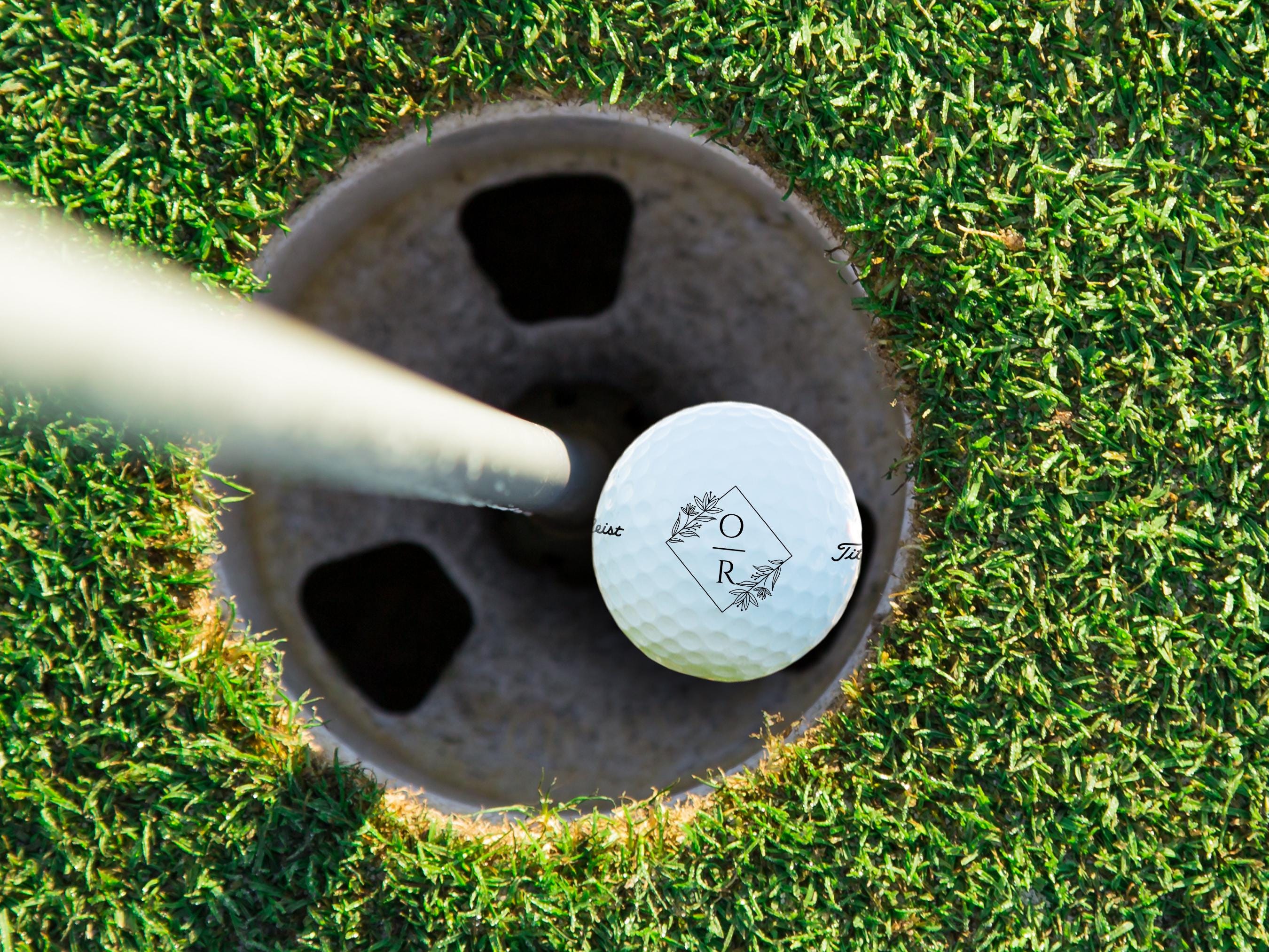 A white golf ball with a monogrammed logo on it, placed on a grassy surface.