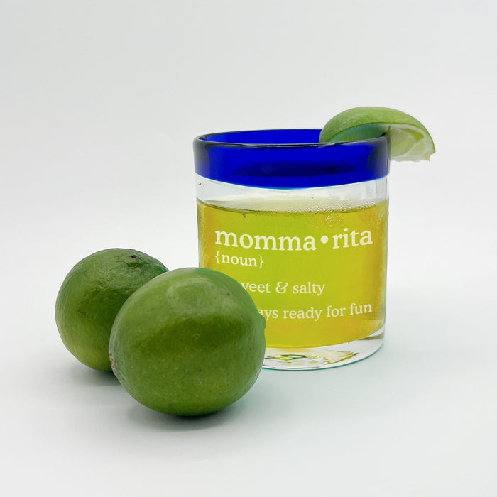 A glass of lemonade with a slice of lime on top, accompanied by two whole limes, on a white background.