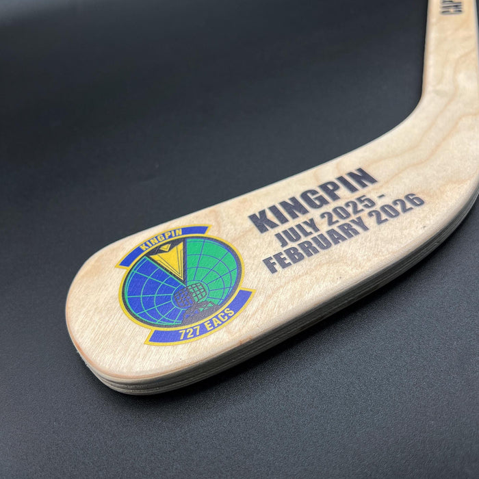 Close-up detail of a hockey stick blade with a full-color printed team logo and custom text, highlighting vibrant UV print on wood grain.
