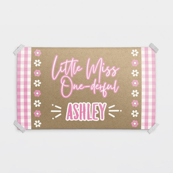 Personalized Little Miss ONE-derful birthday banner printed on brown butcher paper with pink gingham accents, floral details, and custom name personalization.