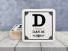 A stack of coasters by a single coaster on a white wooden surface. Coasters shown are customizable. Coasters are designed with a last name and initial.