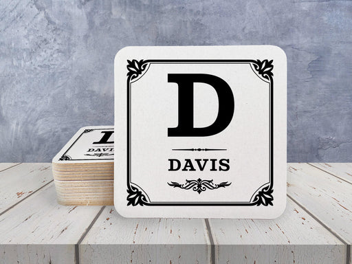 A stack of coasters by a single coaster on a white wooden surface. Coasters shown are customizable. Coasters are designed with a last name and initial.