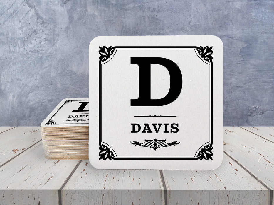 A stack of coasters by a single coaster on a white wooden surface. Coasters shown are customizable. Coasters are designed with a last name and initial.