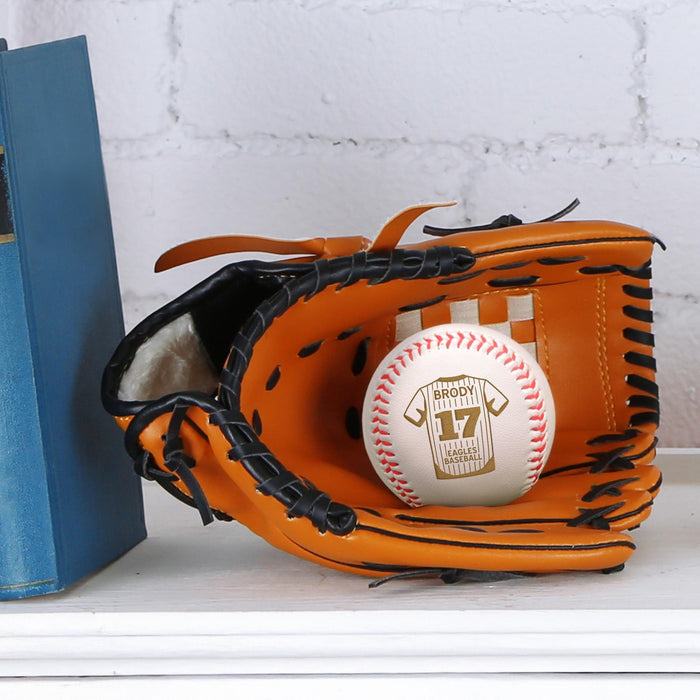 A baseball glove with a personalized baseball inside it, placed on a white surface next to a blue book.