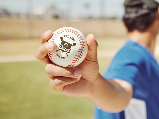 Player holding baseball with #1 Dad design engraved on it.