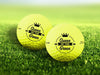 Two personalized yellow golf balls with a Queen of the Green design printed on them, placed on a grassy field.