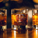 Warm bar-style lifestyle image with glowing ambient lights in the background. The personalized glass is filled with whiskey and ice, highlighting the elegant engraving.