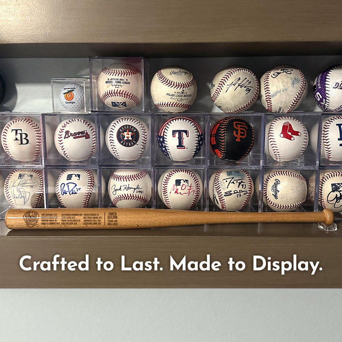 A collection of baseballs and an engraved 18" mini baseball bat displayed on a shelf, with the caption "Crafted to Last. Made to Display."