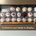 A collection of baseballs and an engraved 18" mini baseball bat displayed on a shelf, with the caption "Crafted to Last. Made to Display."