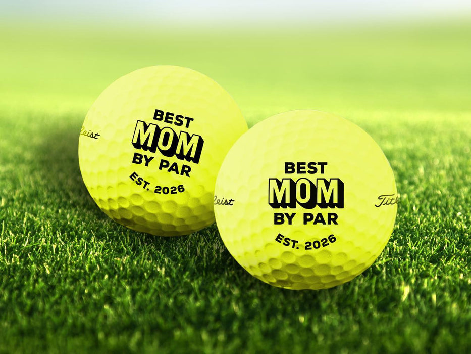 Two yellow golf balls with Best Mom By Par design printed on them, placed on a grassy golf course.