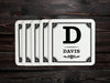 A stack of coasters are spread out on a dark wooden table. Coasters say Davis with decorative frame.