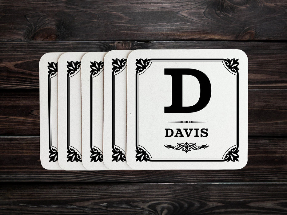 A stack of coasters are spread out on a dark wooden table. Coasters say Davis with decorative frame.