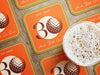 Custom square pulpboard coasters are shown laid out on a wooden surface. A beer mug is shown on top of a few of the coasters. The coaster features design with illustrated golf ball, custom age and year, and vivid orange, cream, and green background.