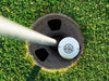 Single white Titleist golf ball with Officially Retired design in golf course hole next to pole surrounded by grass