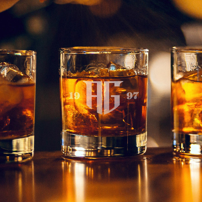 Warm bar-style lifestyle image with soft glowing lights in the background. The personalized monogram glass is filled with whiskey and ice, creating a premium lounge feel.