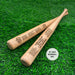Two custom engraved wooden 18" mini baseball bats sit on a grassy surface. One bat has a team logo and roster engraved on it and the other has a team roster engraved on it.