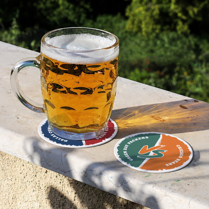 Two-team football coasters displayed outdoors with a beer mug, featuring custom colors and personalized team names.