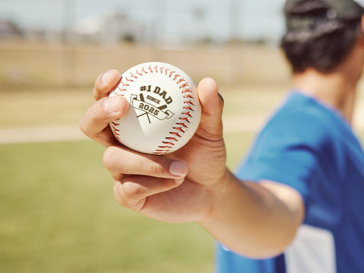 Player holding baseball with #1 Dad design engraved on it.