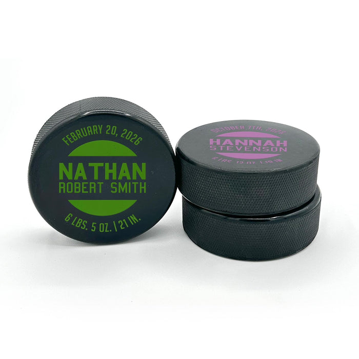 Two personalized hockey pucks showing the UV printed baby birth announcement design in green and pink color options.