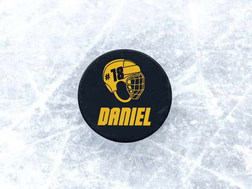 single hockey puck on ice rink with helmet design printed in yellow that says Daniel number 18