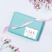 Pastel blue box decorated with a holographic rainbow “With Love” personalized wedding gift tag. A modern and colorful presentation idea for wedding cards and small gifts.