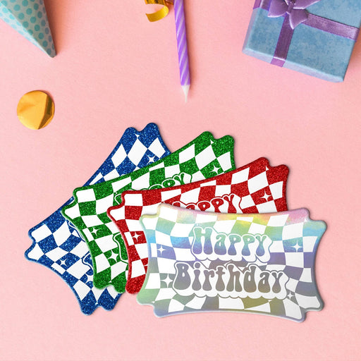 Four groovy gift tags in metallic rainbow, glitter blue, glitter green, and glitter red lying beside colorful gifts and party decorations.
