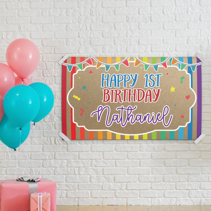 Rainbow first birthday banner displayed on a white brick wall with colorful balloons and party décor.