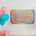 Rainbow first birthday banner displayed on a white brick wall with colorful balloons and party décor.