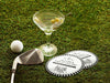 Two custom coasters sit on a grassy golf course next to two martini glasses, a golf club, and a golf ball. The custom coasters feature a golf club lounge design with an illustration of a golf ball on a tee and people cheersing drinks together along with a striped border. The established year, name, lounge name, and tagline can be customized.