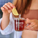 A person is holding a glass mug with a slice of lemon in it, and the mug has a personalized message engraved on it.