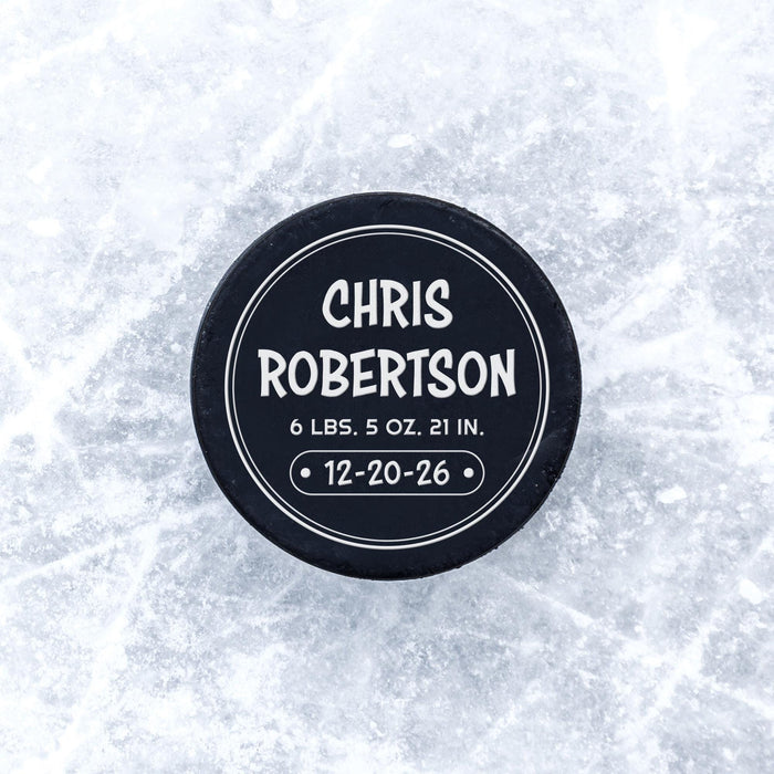 Personalized hockey puck with a white UV printed round birth announcement design displayed on an icy surface.