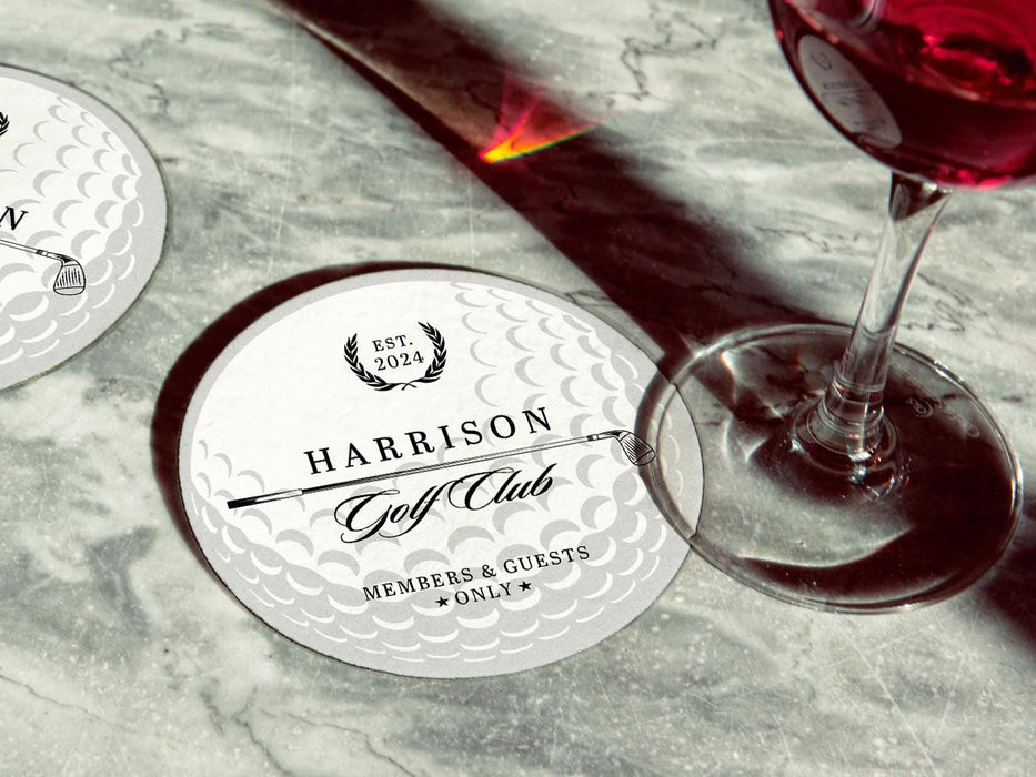 Coaster is shown with a wine glass on top of it and another coaster is off to the side. These feature a golf club and overlayed golf ball design with the text Members & Guests Only between stars. The last name, club name, and established year can be customized.
