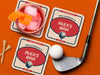 Custom square pulpboard coasters are shown sitting on an orange surface. Golf tees, a golf ball, and a golf club sit beside them. One coaster has a red cocktail on top of it. The custom coasters feature a 19th hole bar design with an illustration of a golf ball. The tagline, bar name, established year, and location can be customized on these.
