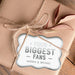 Close-up of a metallic silver “Your Biggest Fans” wedding gift tag tied onto blush fabric wrapping with twine. The personalized foil cardstock tag features custom names in a playful modern font.