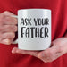 A person in a red sweater holding the “Ask Your Father” mug with both hands. The bright cozy setting adds a fun and playful gift feel.