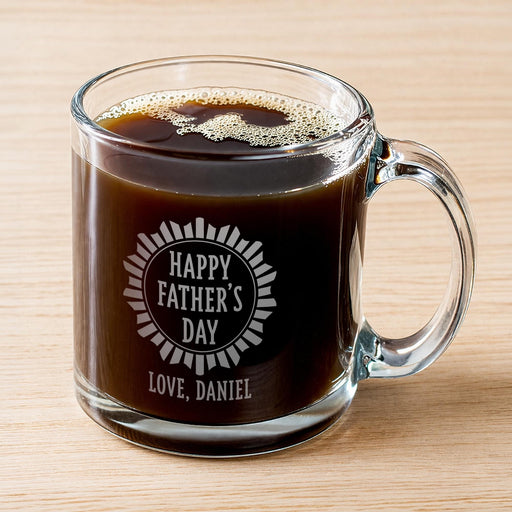 A glass mug filled with a dark liquid, likely coffee, with foam on top. The mug has an engraved message that reads "Happy Father's Day Love, Daniel".