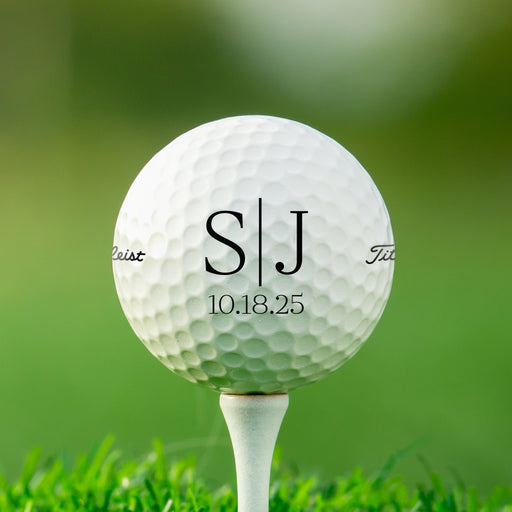 A white golf ball with the initials "SJ" printed on it, placed on a grassy surface.