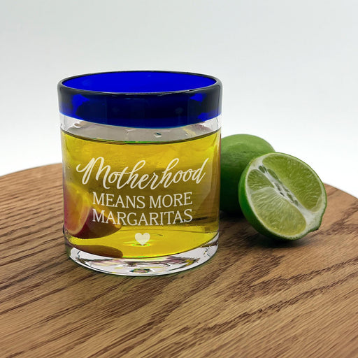 A glass with a blue rim and a yellow liquid inside, accompanied by a lime, all placed on a wooden surface.