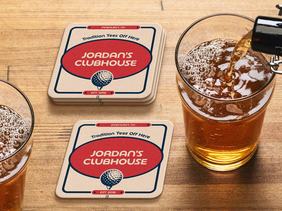 Custom square pulpboard coasters are shown sitting on a wooden table next to two drink glasses. The custom coasters feature a 19th hole bar design with an illustration of a golf ball. The tagline, bar name, established year, and location can be customized on these.
